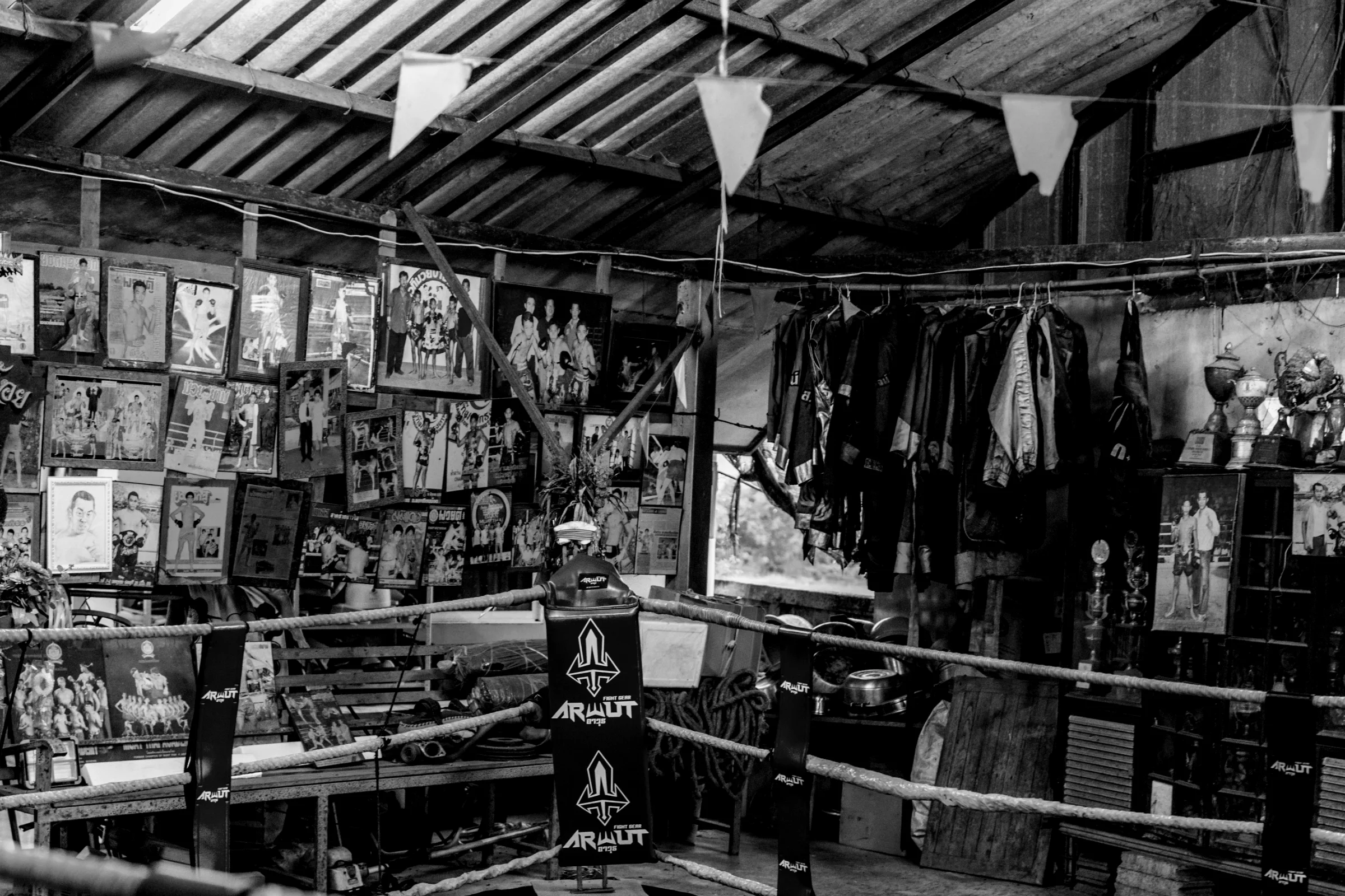 A traditional gym ring beneath a wall of belts and trophies.