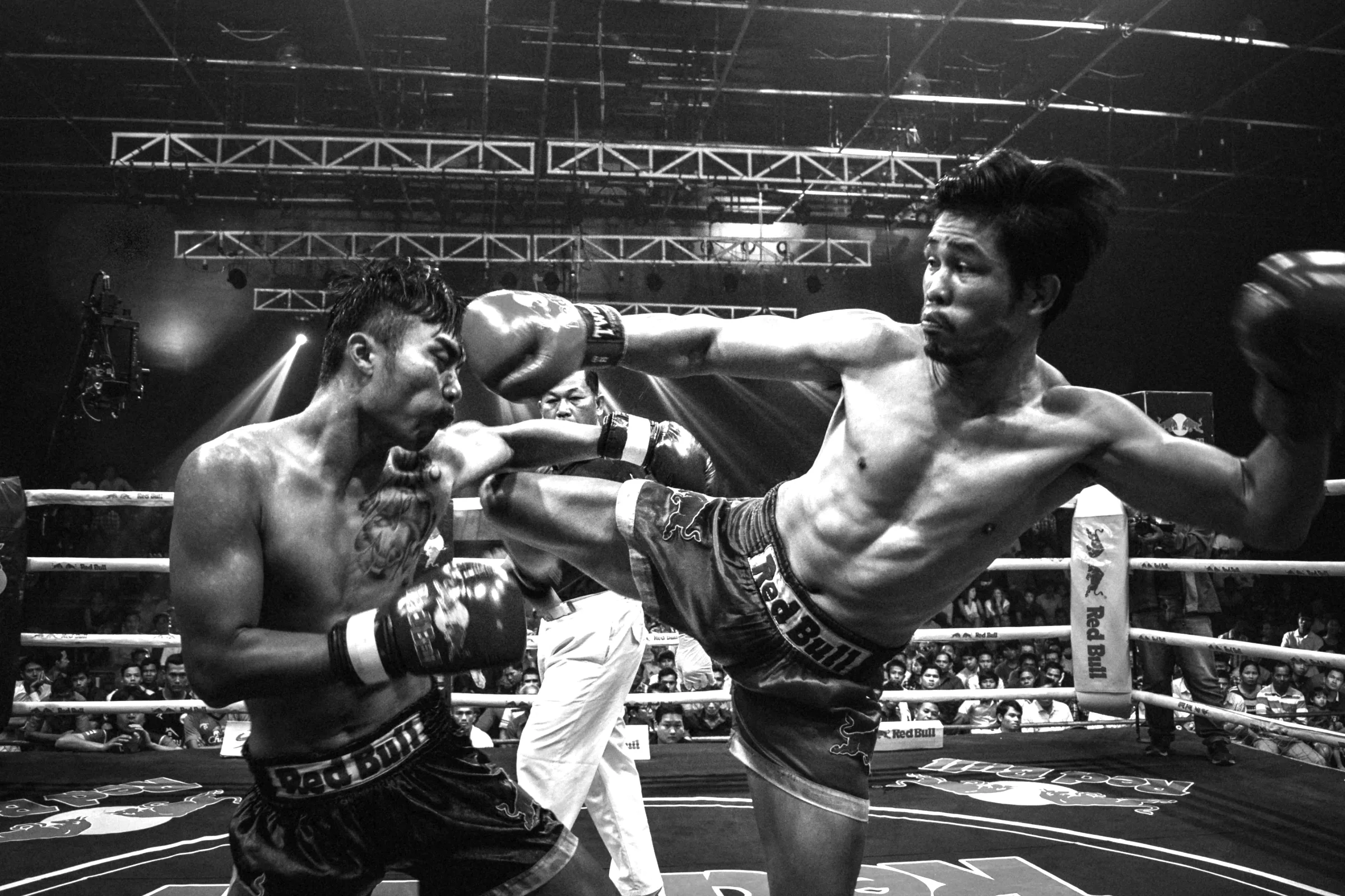Two Muay Thai fighters mid-exchange in a lit ring.