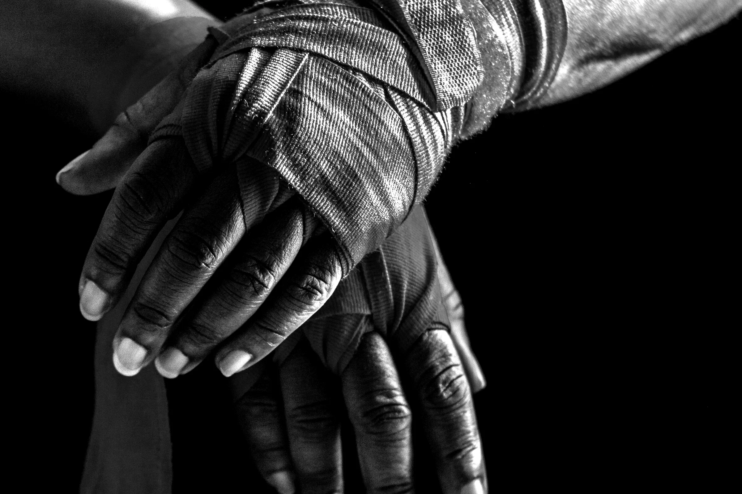 Hands wrapped for training, lit hard against a black background.